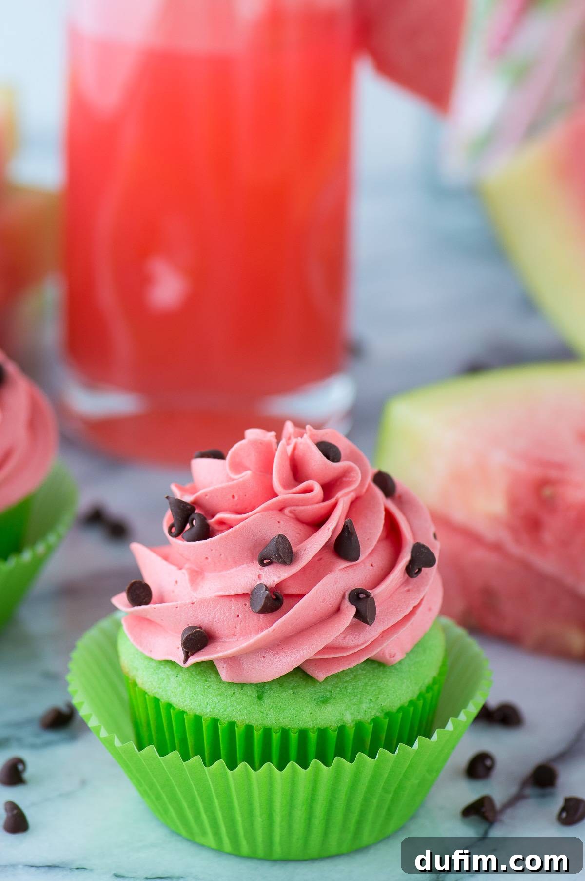 Watermelon Burst Cupcakes 3 A close-up shot of green cupcakes with swirls of pink watermelon frosting and scattered mini chocolate chips on a pristine marble surface.