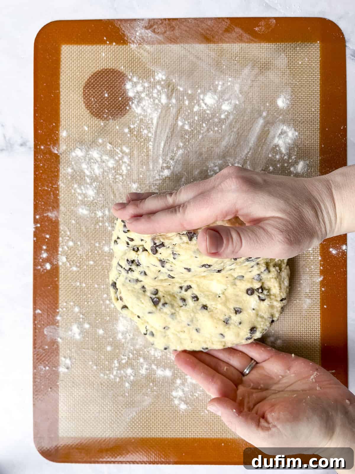 Tender Blueberry Buttermilk Scones 9 Hands gently folding scone dough on a silicone mat to incorporate flour, showing the early lamination process.