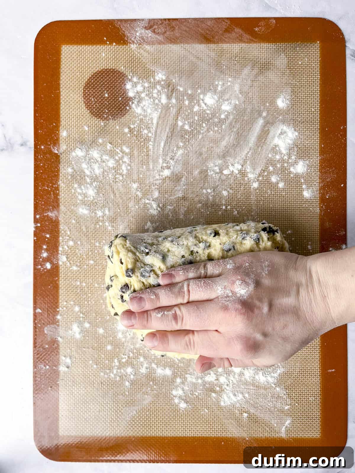 Tender Blueberry Buttermilk Scones 10 Hands continuing to fold and press scone dough on a silicone mat, developing layers for flakiness.