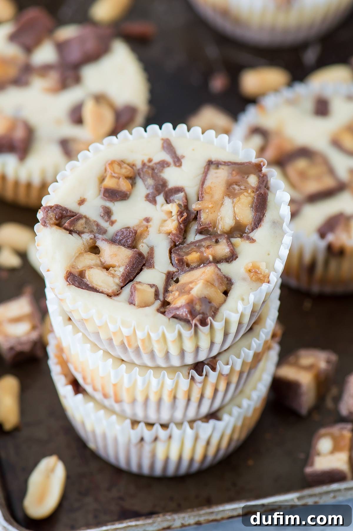 Stacked mini Snickers cheesecakes on a dark metal baking sheet, ready to be served or stored.