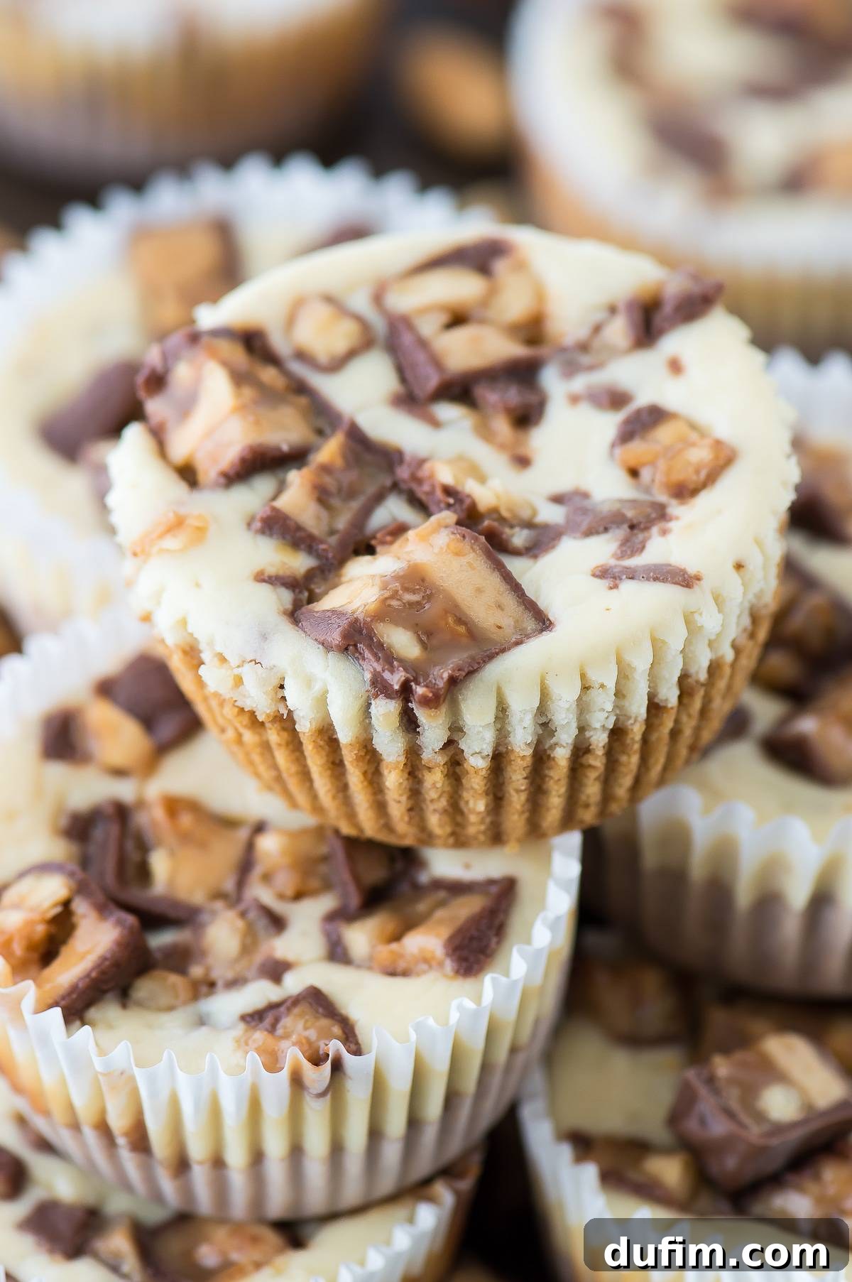 A close-up of a perfectly baked mini Snickers cheesecake, highlighting the texture and candy topping.