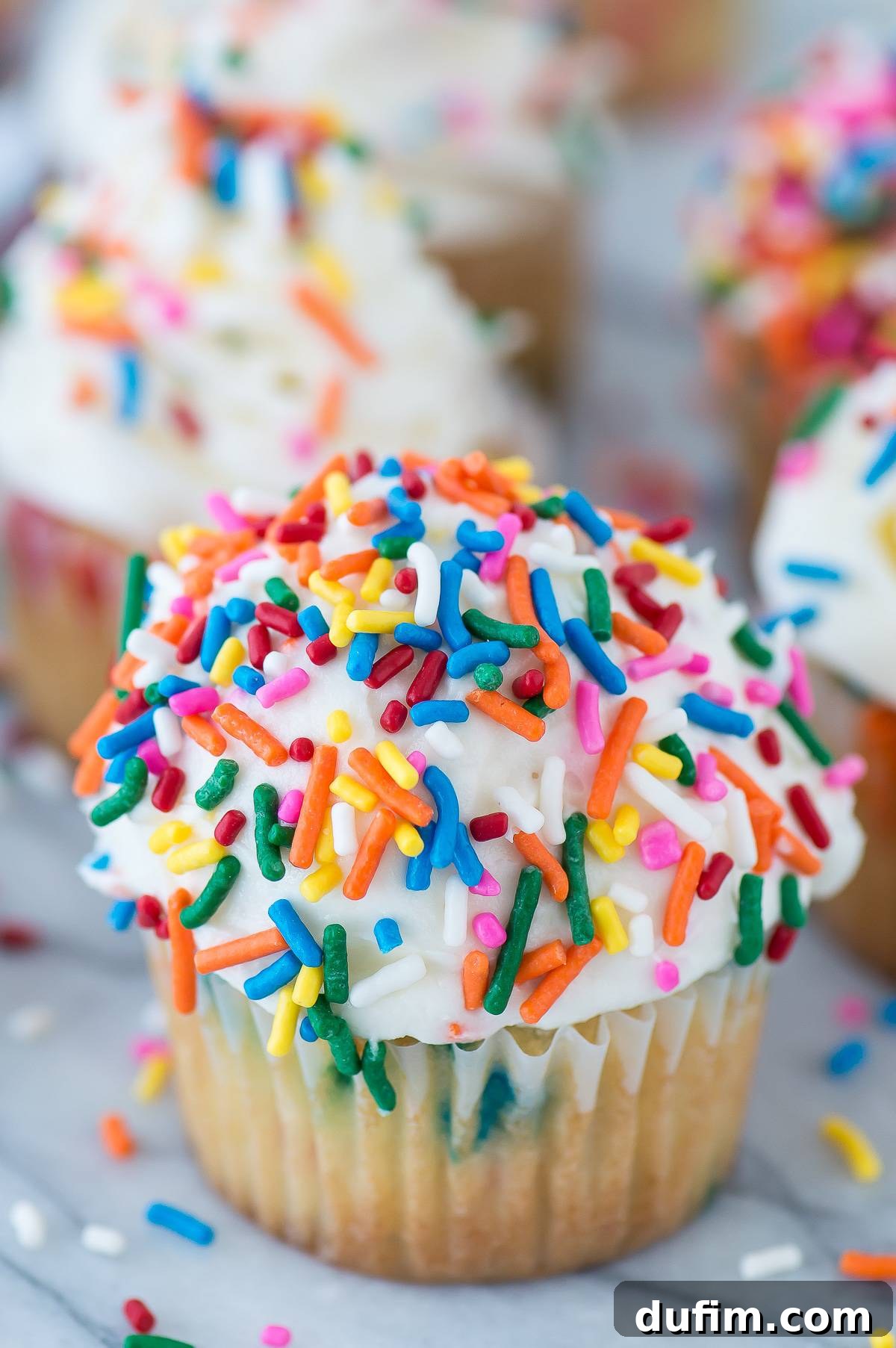 A beautifully frosted funfetti cupcake with white frosting and abundant rainbow sprinkles.