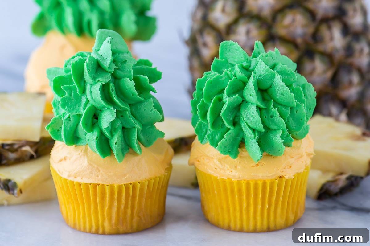 Close-up of three pineapple cupcakes, showcasing the detailed green leaves and textured yellow frosting, capturing the essence of a pineapple.