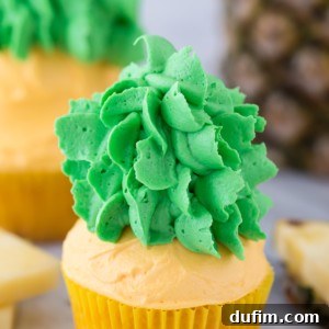 Pineapple cupcakes with vibrant yellow frosting and green leaves, looking like real pineapples. Perfect for tropical parties.