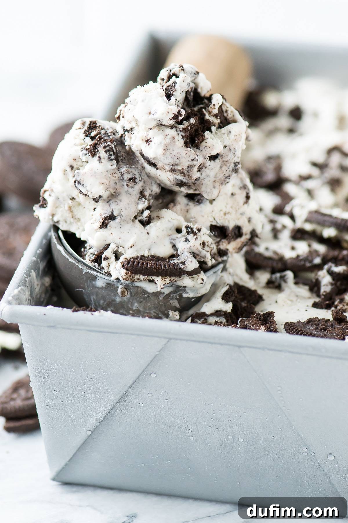 A scoop of homemade Oreo ice cream, generously studded with crushed Oreo cookie pieces, is held aloft, ready to be enjoyed. The texture appears smooth and inviting.