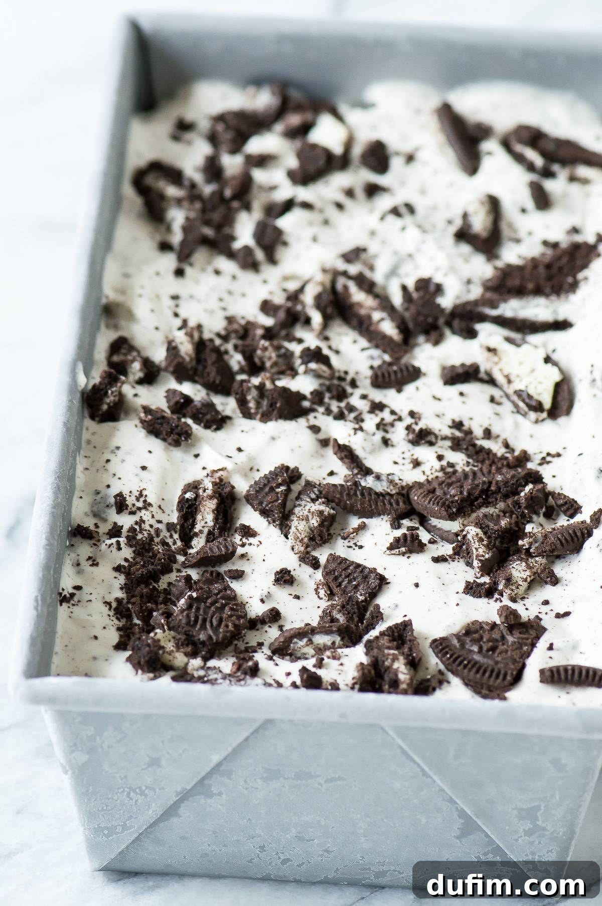 Homemade Oreo Ice Cream rests invitingly in a metal loaf pan, showcasing its rich, creamy texture and abundant cookie pieces, ready for scooping.
