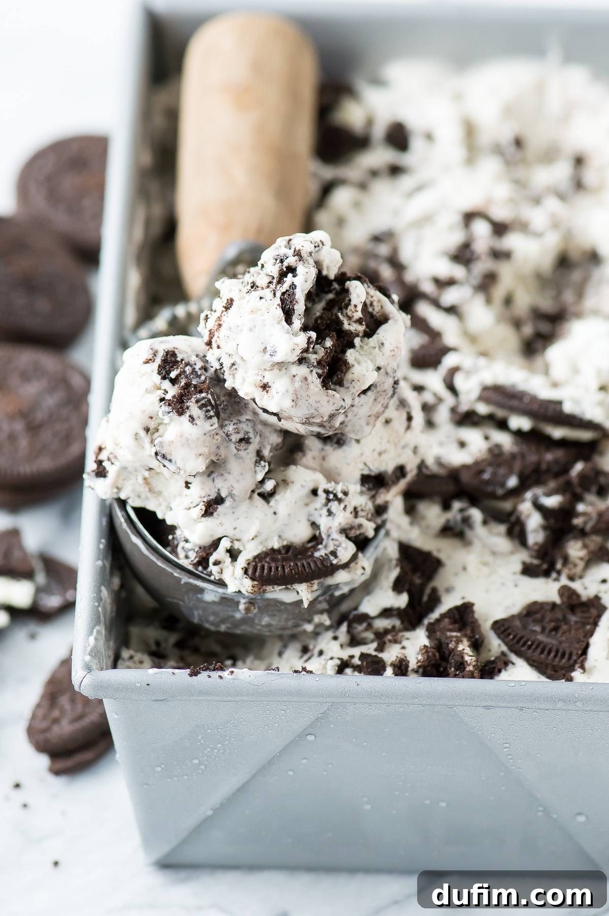 A serving of easy Oreo Ice Cream is being scooped out of a metal loaf pan, revealing its delightful texture and cookie chunks, ready to be served.