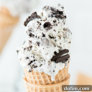 A close-up of a waffle cone filled with Oreo ice cream, showing visible chunks of chocolate sandwich cookies mixed into the creamy white ice cream.
