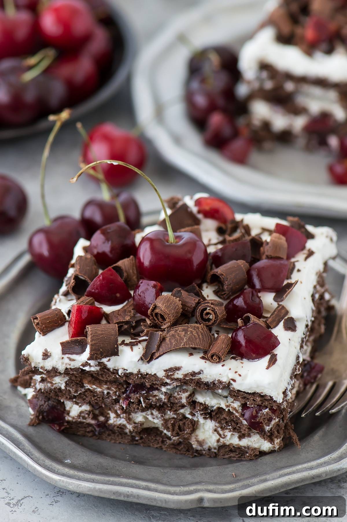 A perfectly cut slice of Black Forest Icebox Cake, showing the beautiful layers of chocolate crackers, white cream, and red cherries, garnished with chocolate shavings.