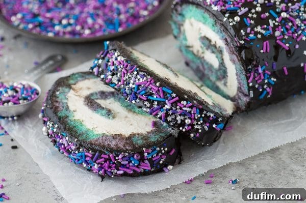 A stunning cross-section of the galaxy cake roll, showcasing the intricate multi-colored swirls of the cake and the creamy white filling, topped with dark ganache and sprinkles.