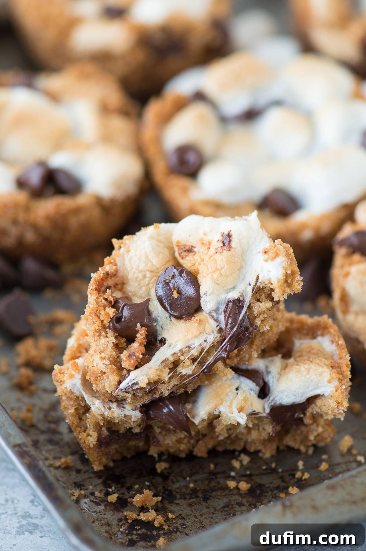 Smores Delight Cups 7 Two half-eaten, delicious indoor S’mores Cups, revealing their gooey layers of chocolate and marshmallow, surrounded by more homemade s'mores cups on a baking dish.