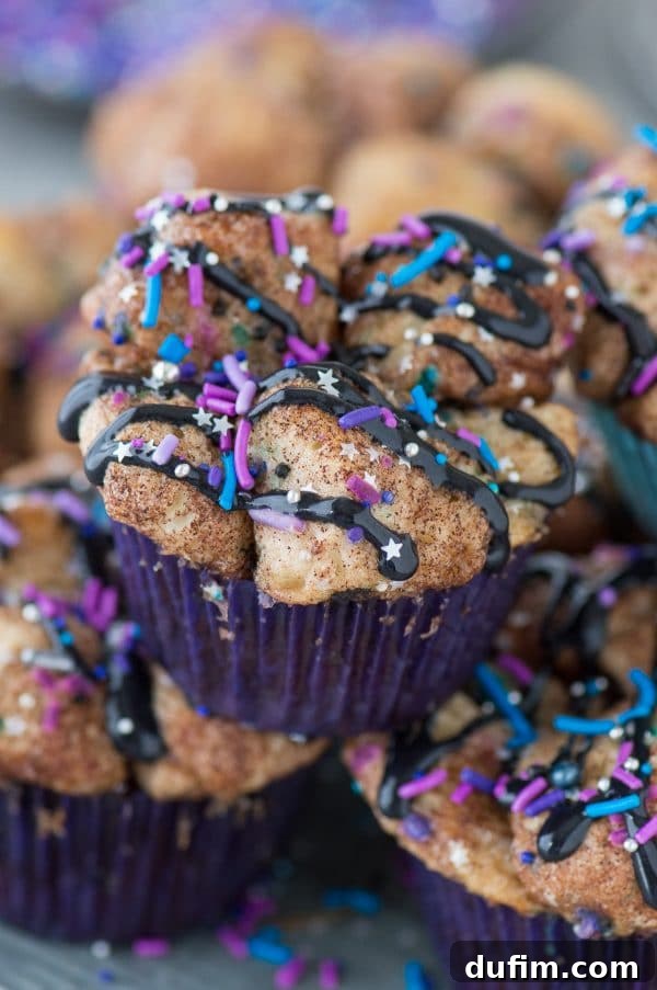 A platter of beautifully decorated Galaxy Monkey Bread Muffins, featuring black cream cheese glaze and diverse sprinkles, ready to be enjoyed.