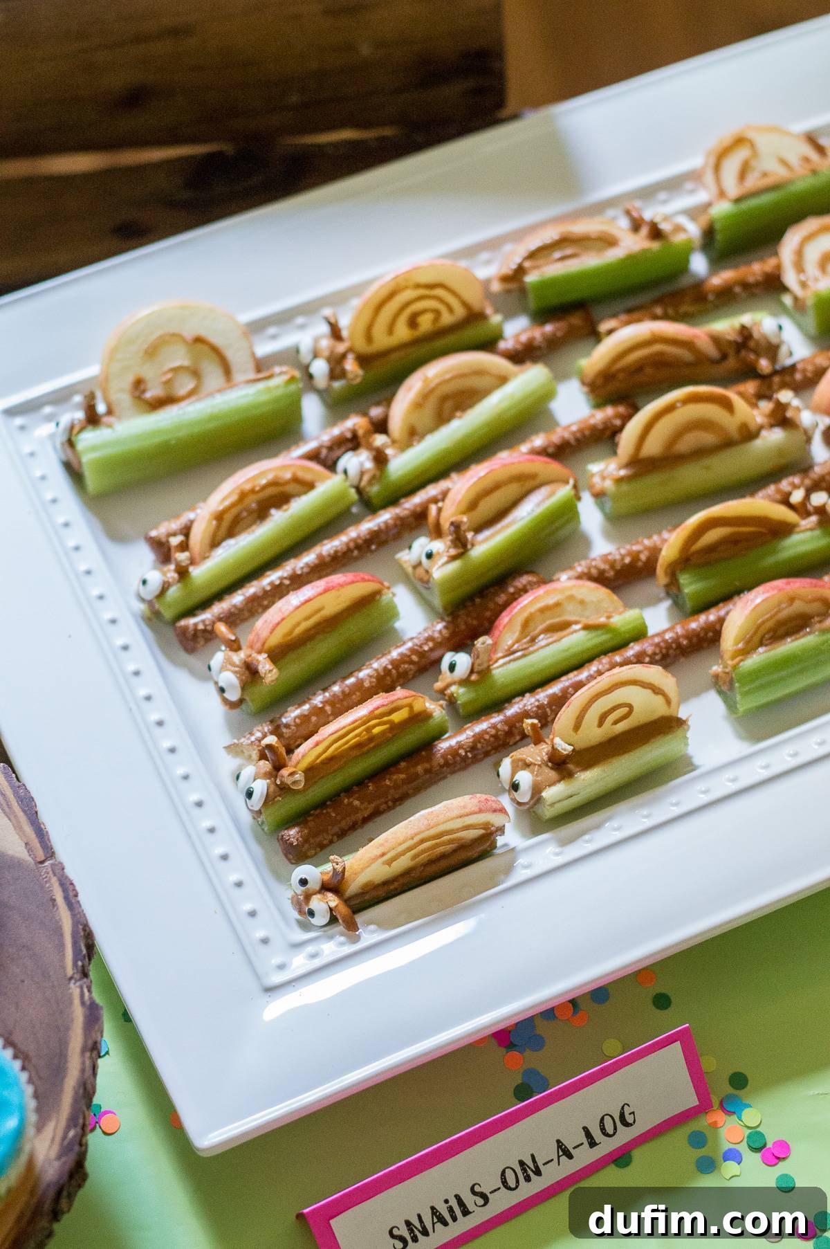 A Dream Fulfilled Adoption Party 11 Close-up of 'Snails on a Log', a creative and healthy snack made with crisp celery, creamy peanut butter, a slice of apple for the shell, pretzel pieces for antennae, and tiny candy eyeballs.