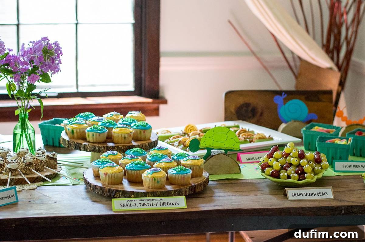 A Dream Fulfilled Adoption Party 4 A close-up of the 'Worth the Wait' party food table, showcasing a variety of slow animal themed snacks, including inchworm skewers, sloth marshmallows, and a fruit turtle. Hand-drawn animal cutouts are visible as part of the decoration.