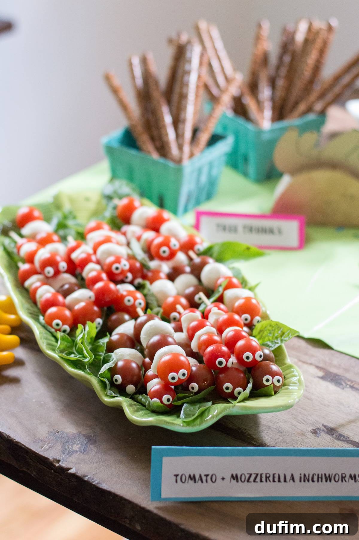 A Dream Fulfilled Adoption Party 5 Detailed shot of vibrant tomato and mozzarella inchworm skewers with candy eyeballs, artfully displayed on a lush green platter with fresh basil leaves for a pop of color.