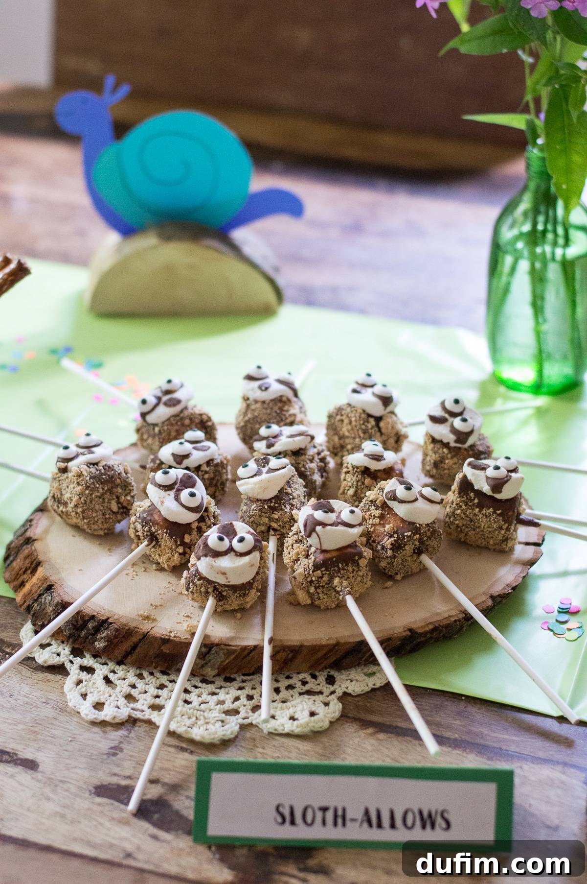 A Dream Fulfilled Adoption Party 6 Close-up of 'Sloth-allows' - large marshmallows expertly dipped in melted chocolate and coated with crushed graham crackers, featuring a smaller marshmallow for the sloth's face and candy eyes, resting on a rustic serving tray.