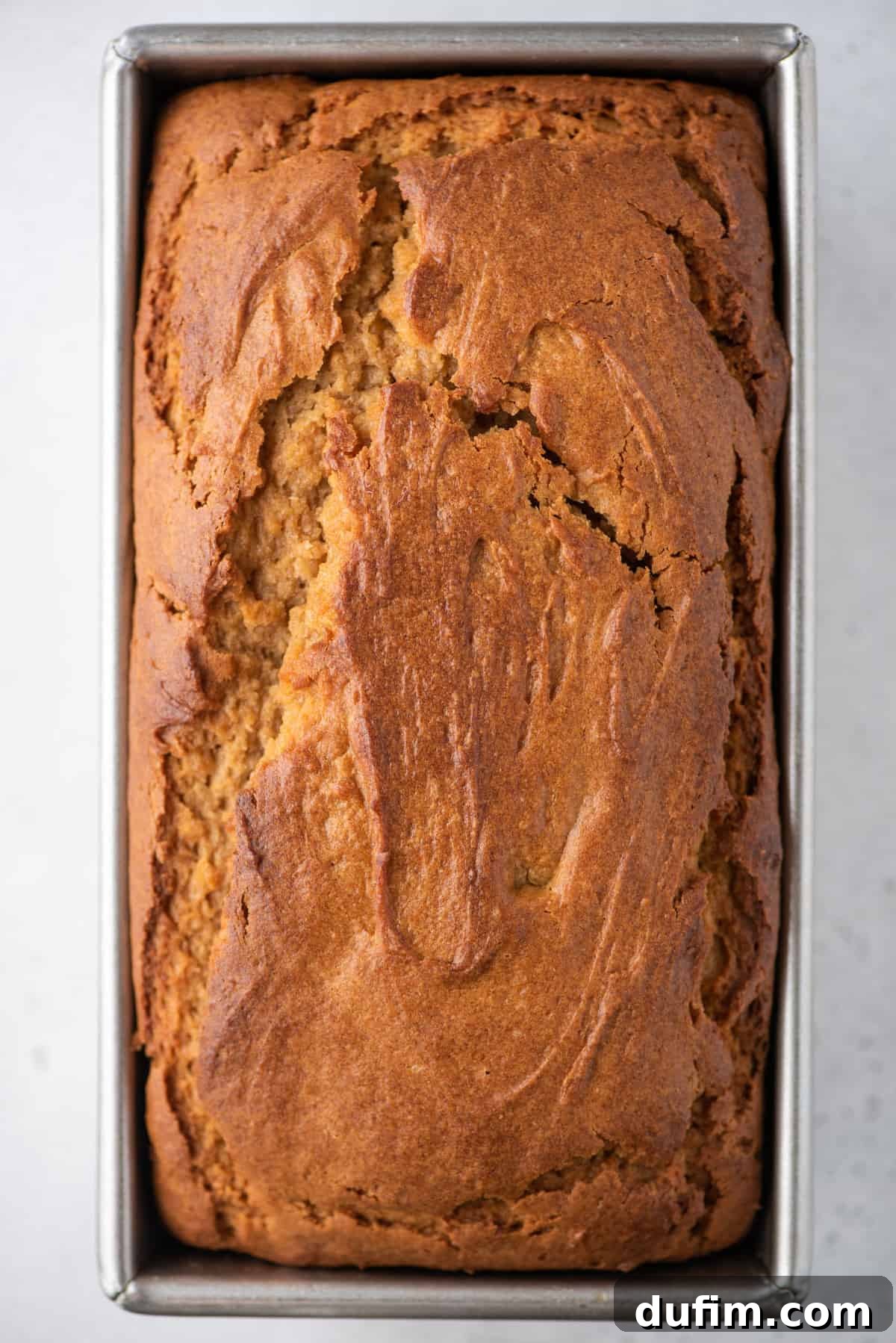 Freshly baked peanut butter bread still in the metal loaf pan, resting on a white background