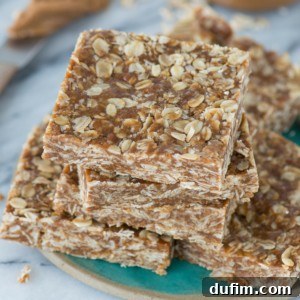 A stack of homemade oatmeal peanut butter biscoff bars sits on a plate. The square-shaped bars are filled with visible oats and cookie spread, giving them a hearty, chewy appearance.