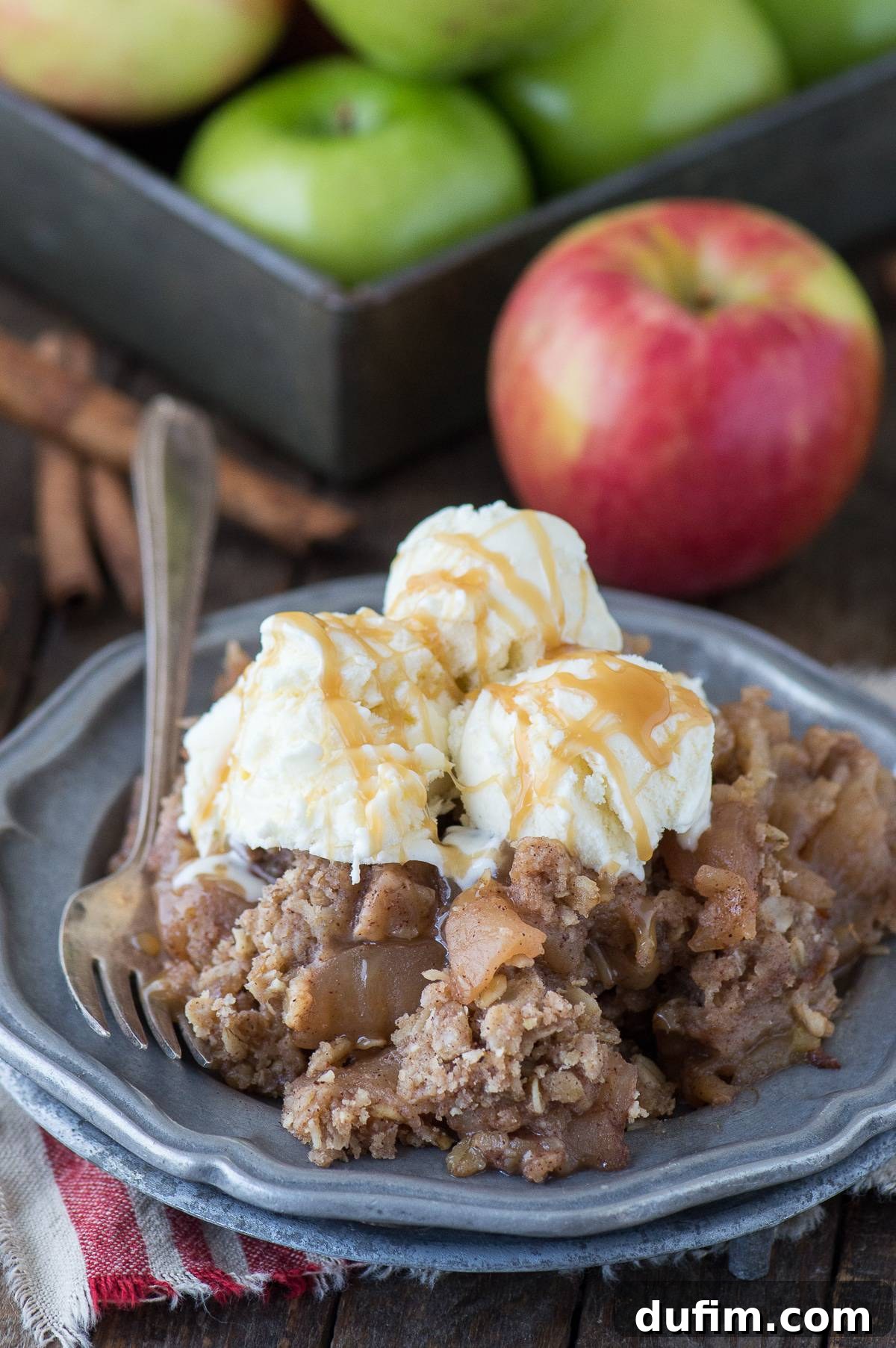 Scoop of crock pot apple crisp with three scoops of vanilla ice cream on a metal plate, drizzled with caramel sauce.