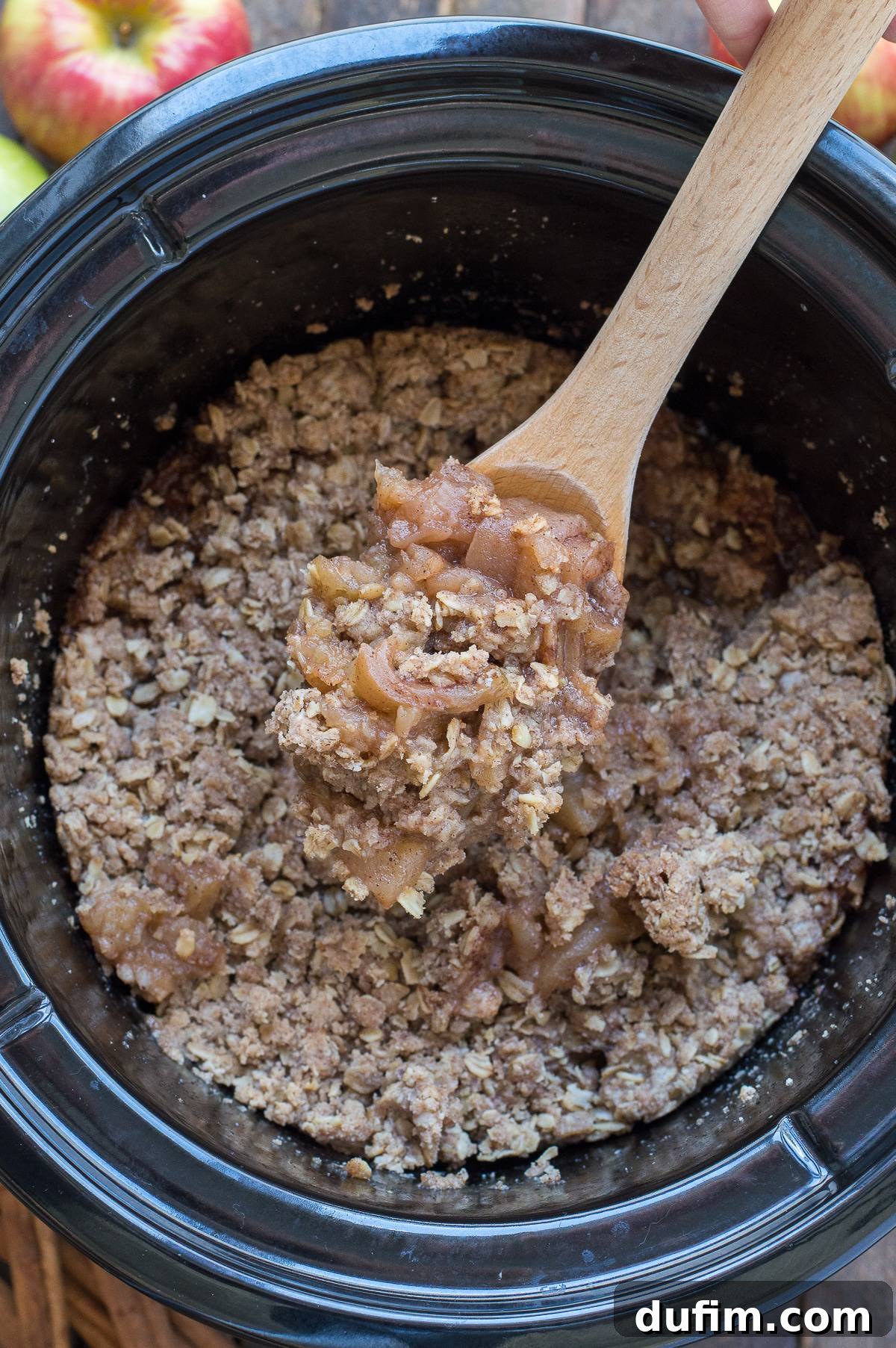 Crock pot apple crisp served directly in a black crock pot with a wooden spoon.