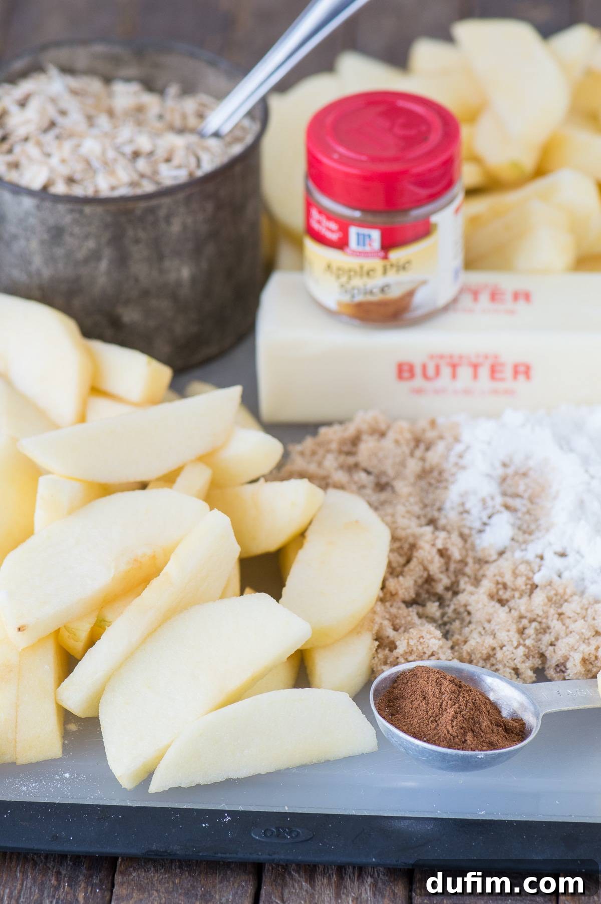 Ingredients to make crock pot apple crisp, including fresh apples, butter, brown sugar, cinnamon sticks, and rolled oats, arranged on a rustic surface.