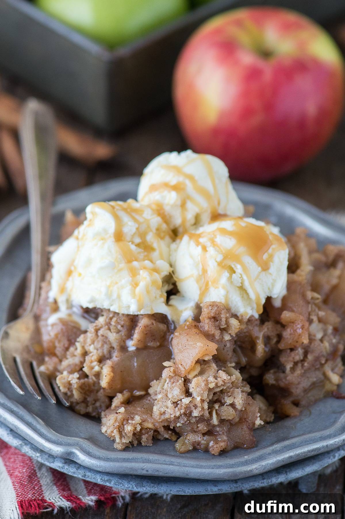 A serving of crock pot apple crisp with three scoops of vanilla ice cream on a metal plate, ready to be enjoyed.
