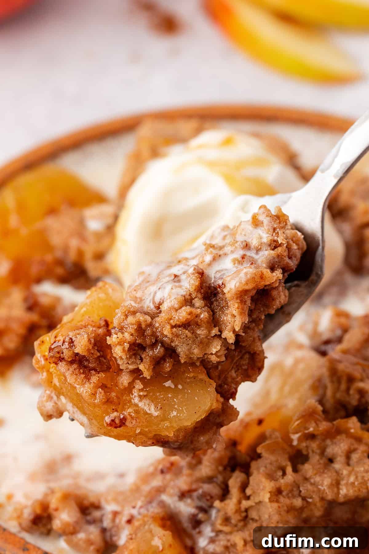 A close-up of a fork holding a bite of apple dump cake with tender apples and crumbly topping. A scoop of melting vanilla ice cream mingles with the dessert on a ceramic plate, creating an irresistible blend.