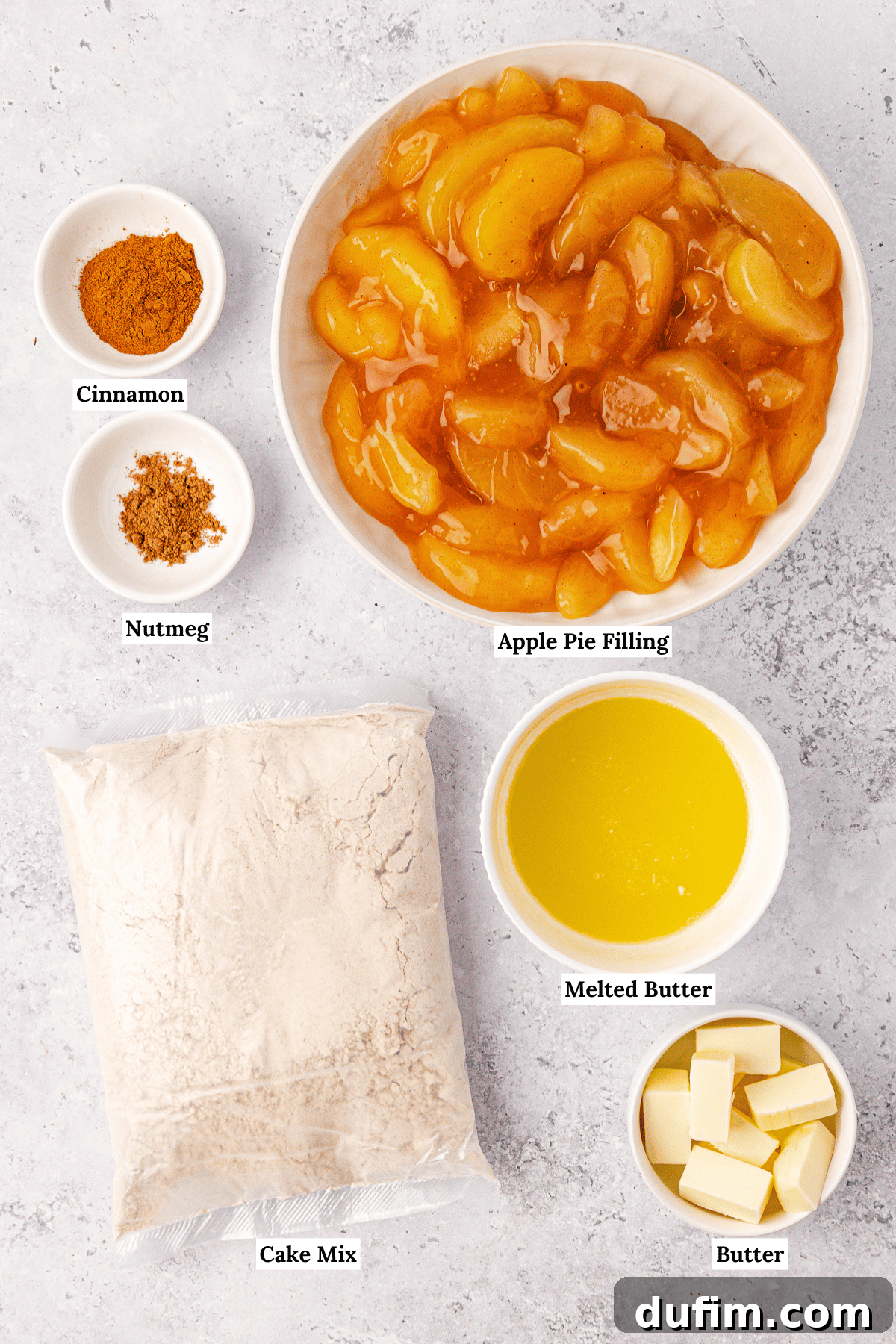 Top view of ingredients for an apple dump cake: a bowl of apple pie filling, small bowls of cinnamon and nutmeg, melted butter in a bowl, a bag of cake mix, and a bowl of sliced butter, all labeled on a light surface.