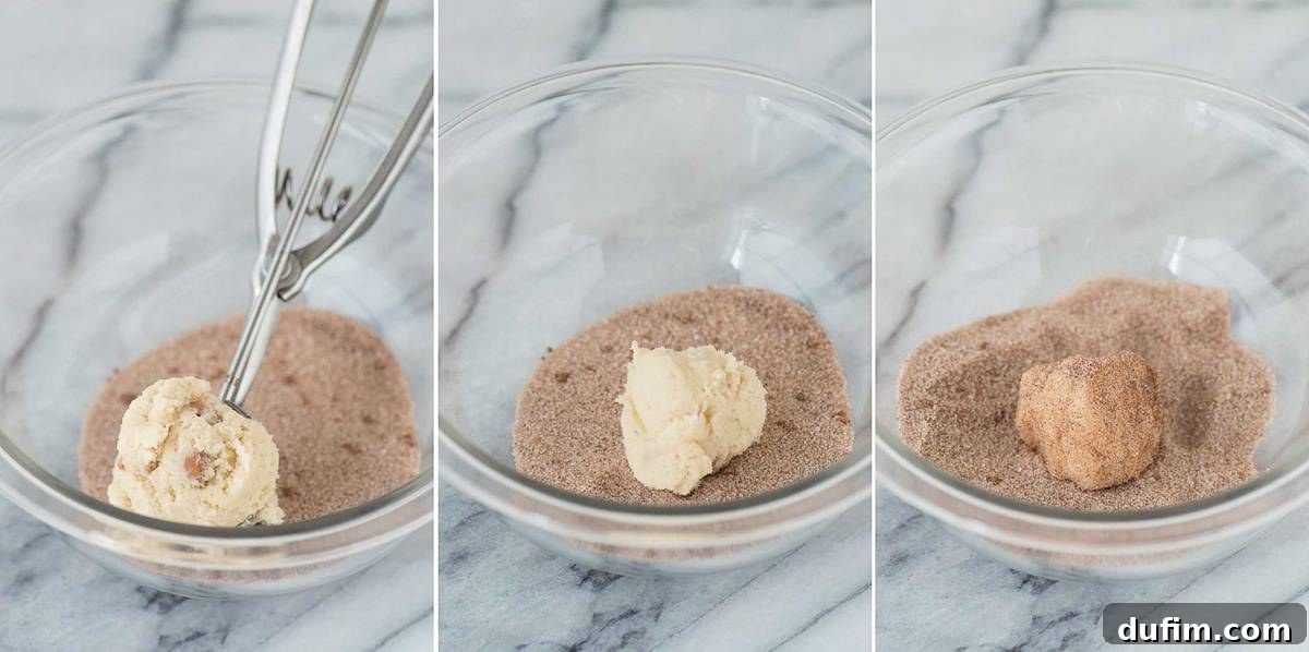 Hands rolling a ball of snickerdoodle cookie dough in a mixture of cinnamon and sugar in a clear glass bowl, preparing it for baking.