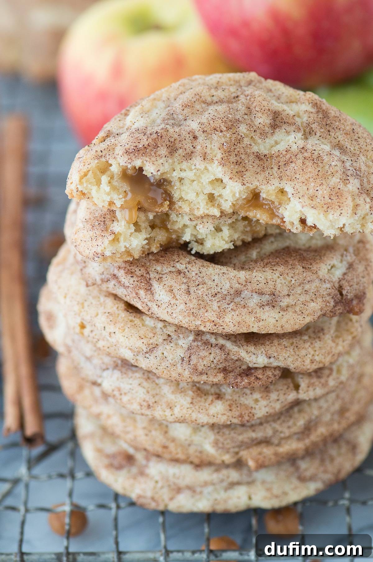 Two stacks of caramel apple snickerdoodle cookies on a metal cooling rack, with an autumnal background of fresh apples, emphasizing the fall theme.