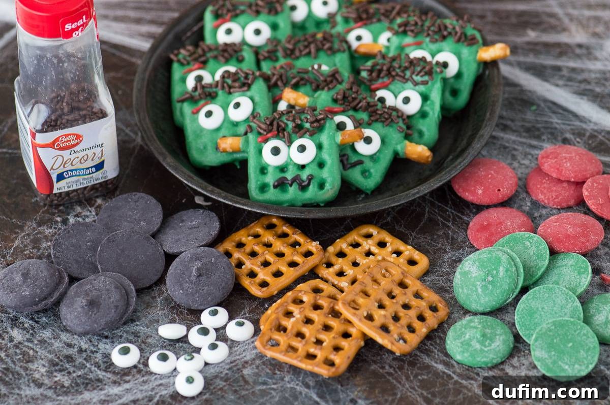 Ingredients laid out for making Frankenstein pretzels, including black, red, and green candy melts, square pretzels, candy eyeballs, and brown sprinkles, all displayed on a dark background, ready for assembly.