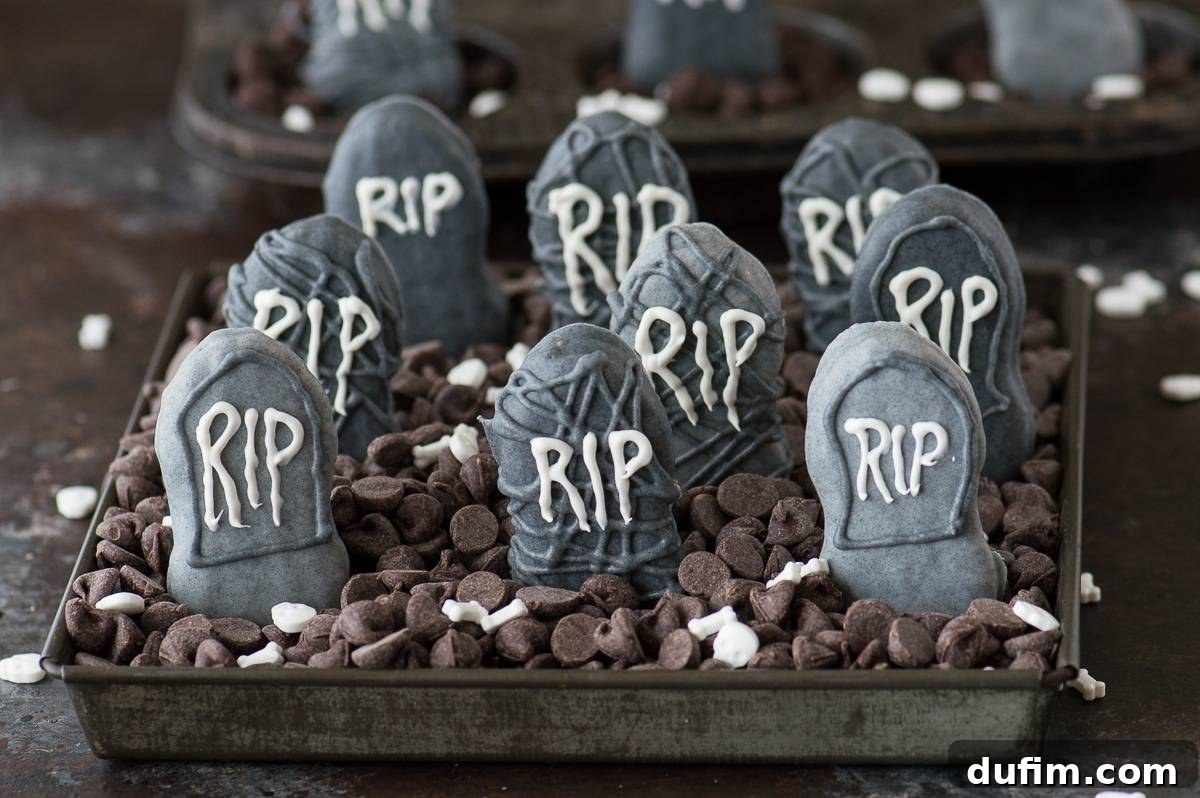 Eerie Nutter Butter Graveyard Treats 3 Close-up of a Nutter Butter Tombstone treat with 'RIP' written on it, against a blurred background of a chocolate chip graveyard.