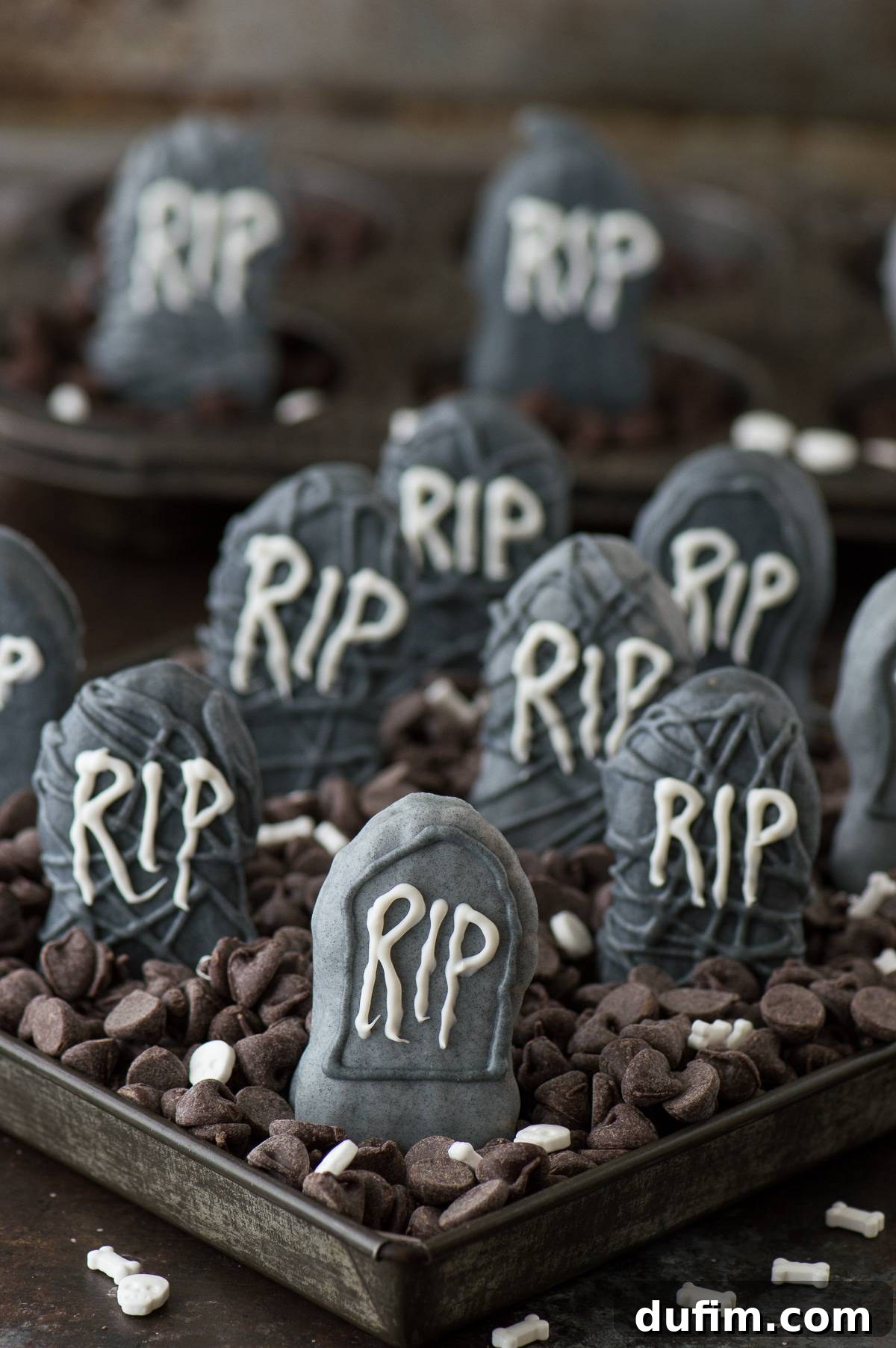 Eerie Nutter Butter Graveyard Treats 5 A hand dipping a Nutter Butter cookie into melted gray chocolate to create a tombstone treat.