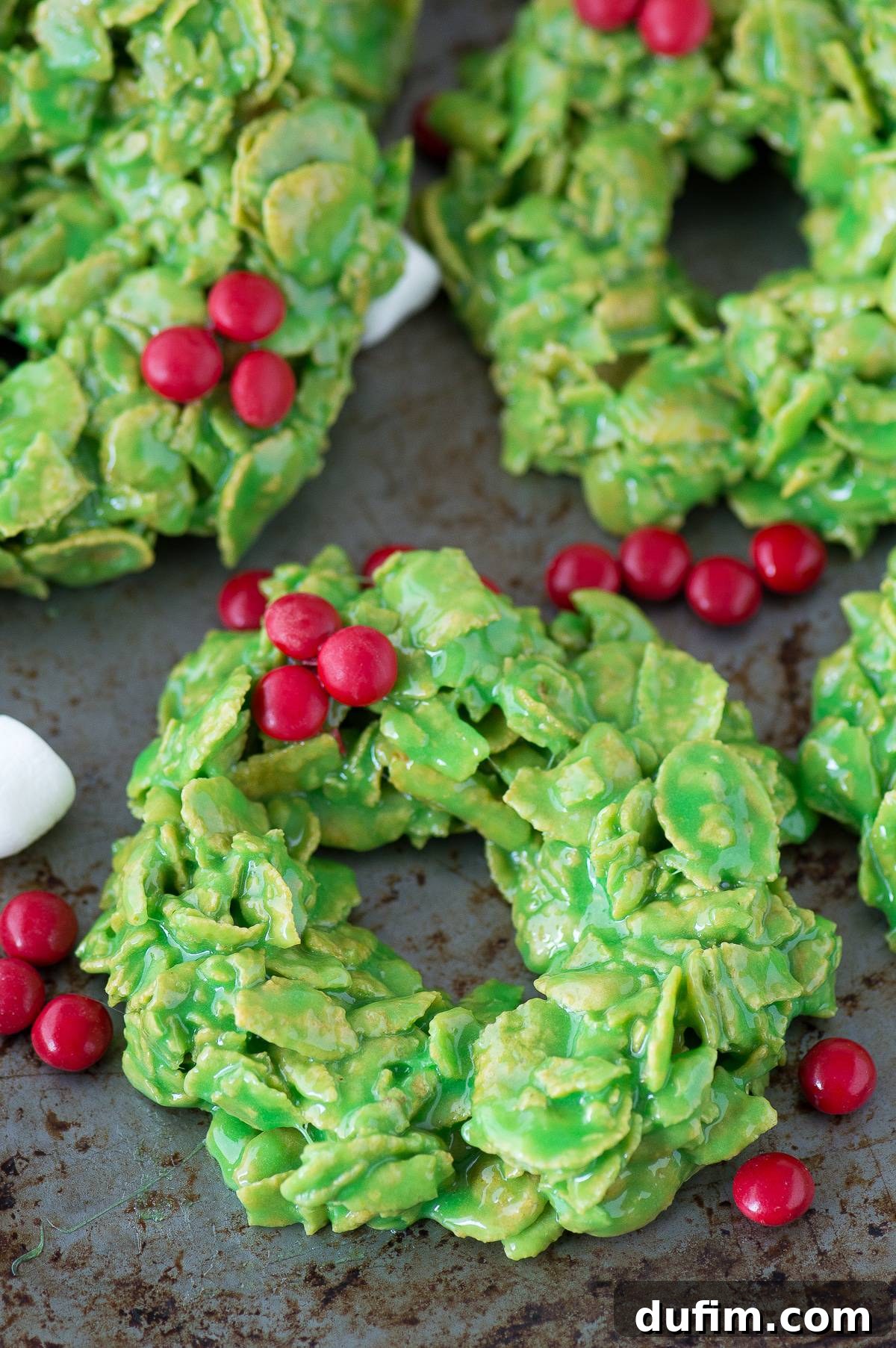 Golden No-Bake Wonders 12 Several finished green Christmas wreath cookies, brightly decorated with red M&Ms and no bows, neatly arranged on a shiny metal surface, awaiting enjoyment.