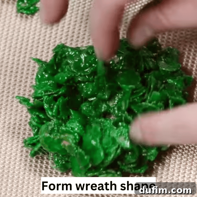 Golden No-Bake Wonders 9 Hands carefully shaping a ball of green cornflake mixture into a flat, round disk on a baking sheet, illustrating the first step in forming a wreath shape.