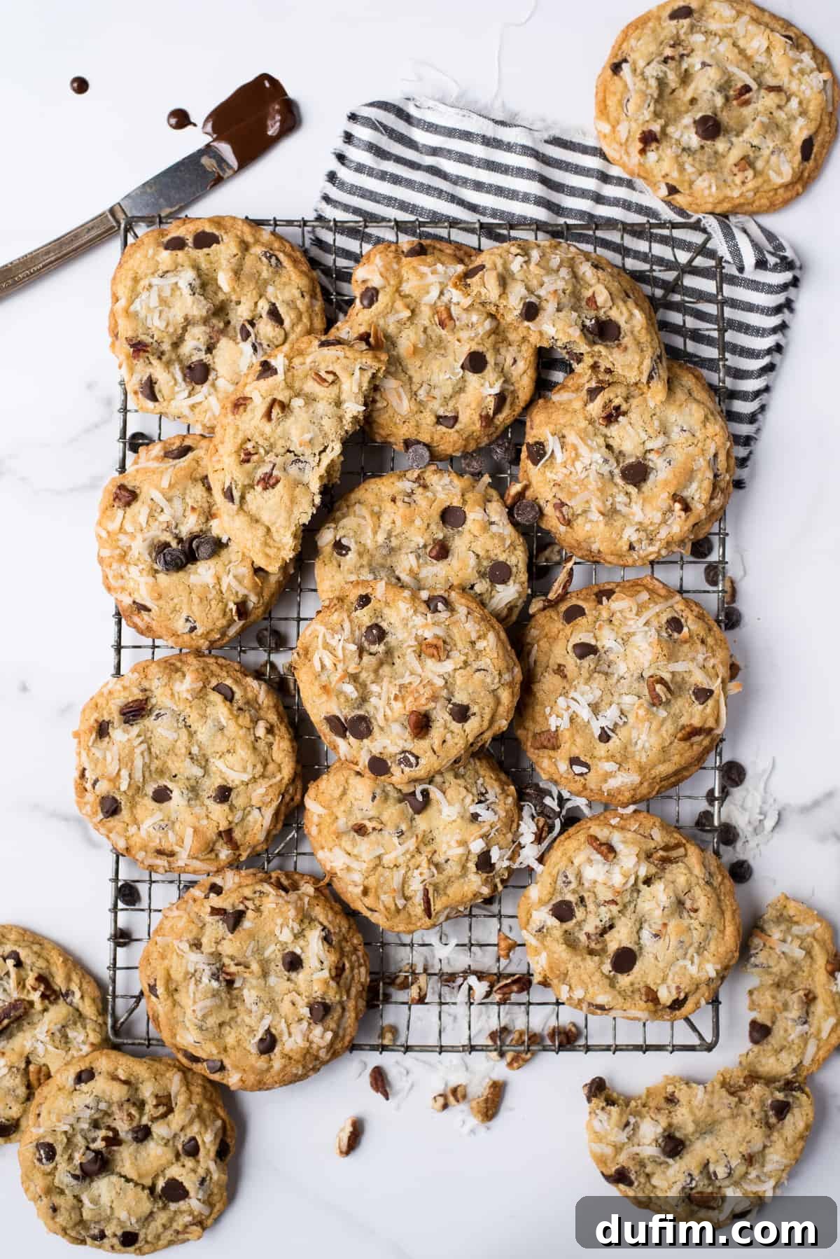 Freshly baked cowboy cookies arranged on a metal cooling rack with a blue striped towel underneath, ready to be enjoyed.