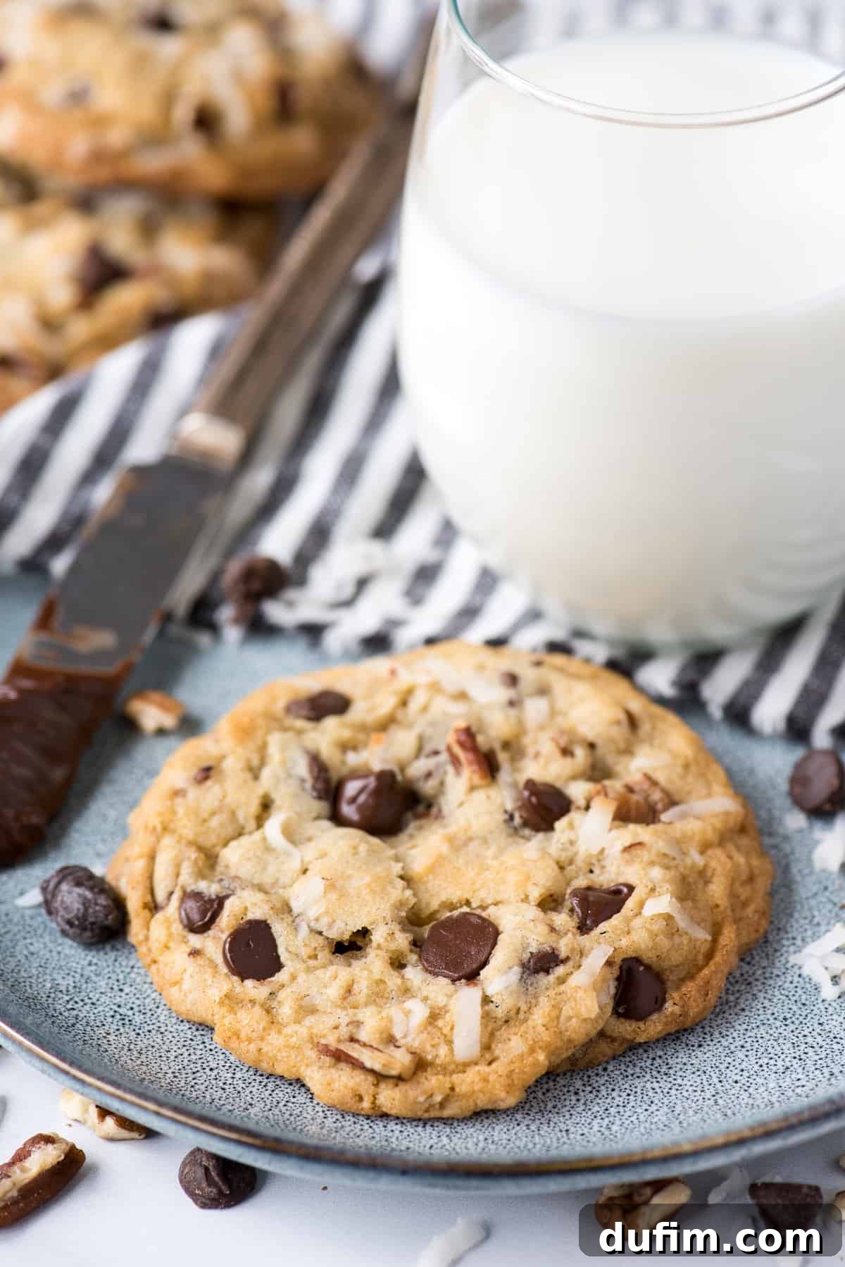 A single cowboy cookie artfully placed on a blue speckled plate, with a refreshing glass of milk softly blurred in the background, inviting a delightful snack.