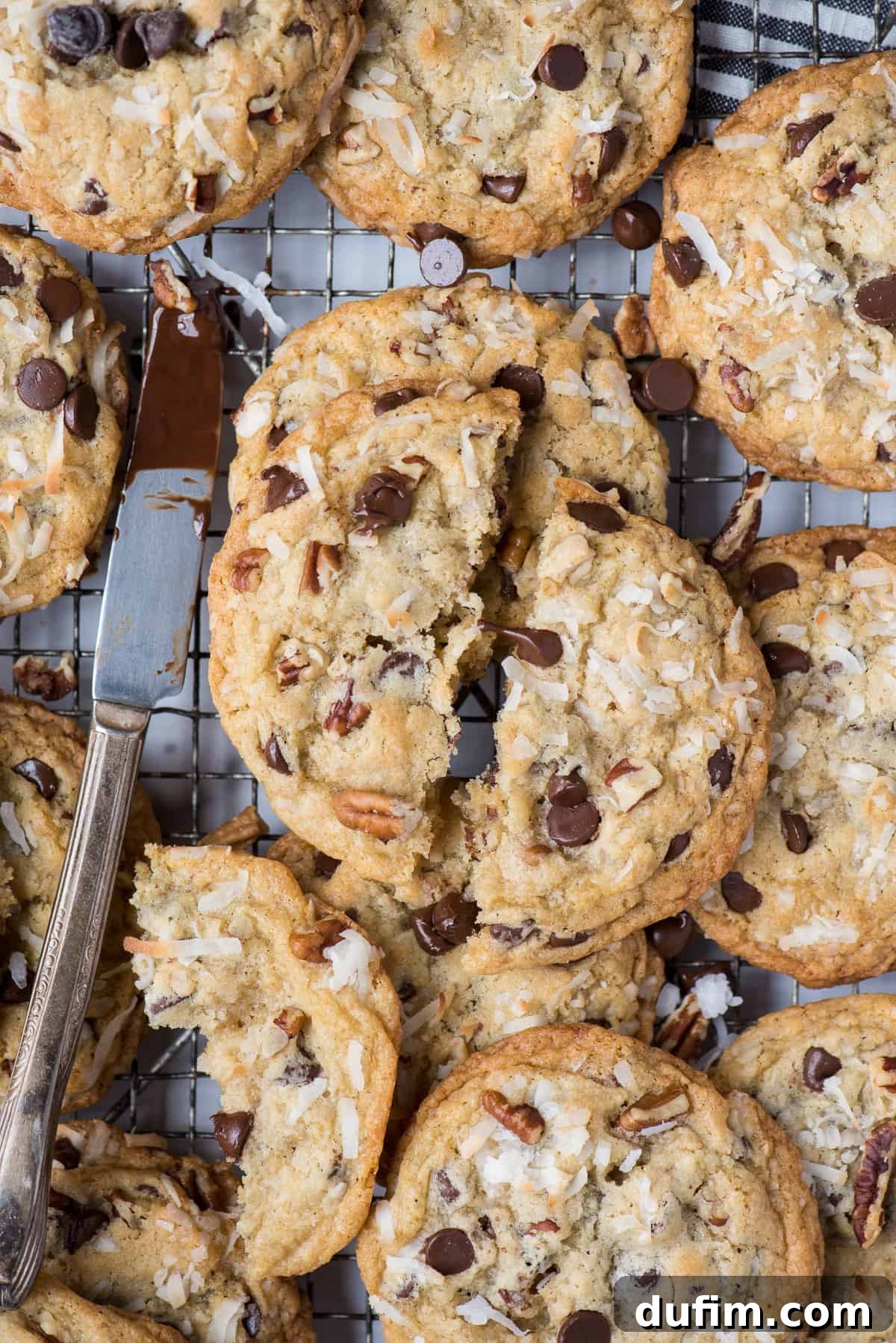 Several warm Cowboy Cookies cooling on a wire rack, with a small knife smudged with chocolate nearby, hinting at their rich flavor.