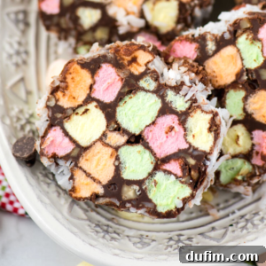 Close-up of colorful marshmallow slices, reminiscent of church window cookies, coated in chocolate and rolled in shredded coconut, served on a decorative white plate.