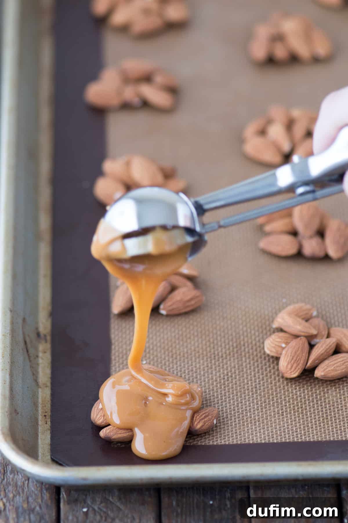 Williams Sonoma's Iconic Sticky Paws, Perfected at Home 4 Spoon drizzling melted caramel over almond clusters on parchment paper, showing the process of making Sticky Paws.