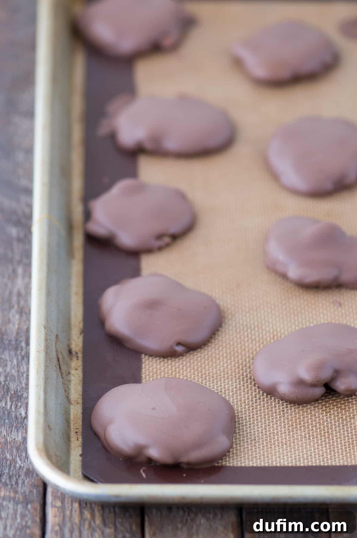 Williams Sonoma's Iconic Sticky Paws, Perfected at Home 8 Finished almond caramel chocolate clusters cooling on a silicone baking mat, showing the full batch.