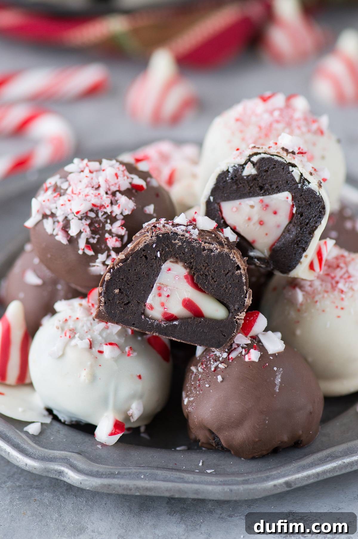 Two Peppermint Oreo Balls cut open on a metal plate, revealing the creamy chocolate filling and the hidden peppermint Hershey's Kiss inside, surrounded by whole truffles.