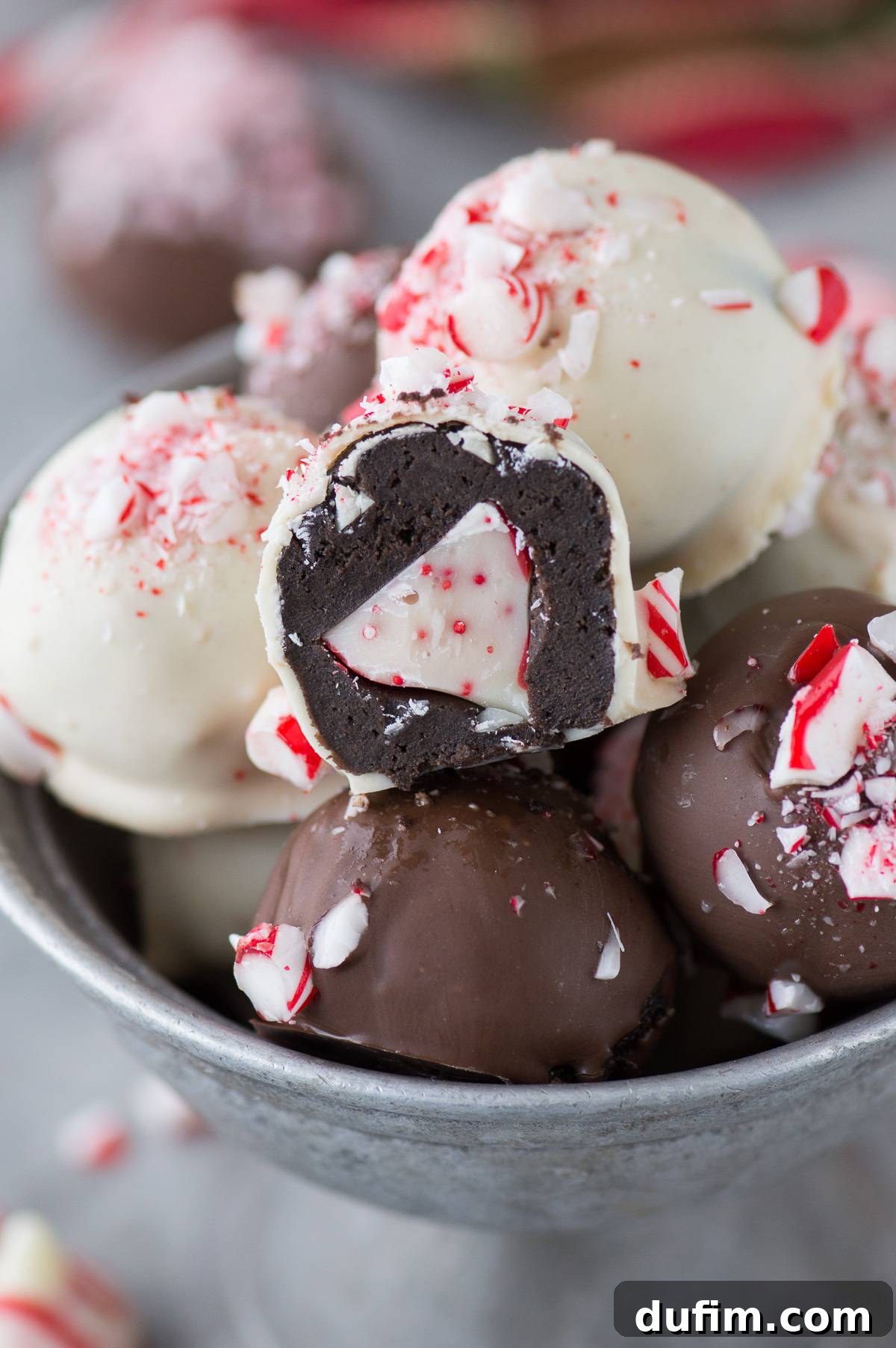 A delicious Peppermint Oreo Ball cut in half to showcase the hidden peppermint Hershey's Kiss, surrounded by other truffles in a metal bowl.