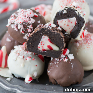 A plate of chocolate and white chocolate truffles, some cut open to reveal a dark chocolate filling with a peppermint candy center. Crushed peppermint pieces are sprinkled on top for a festive touch.
