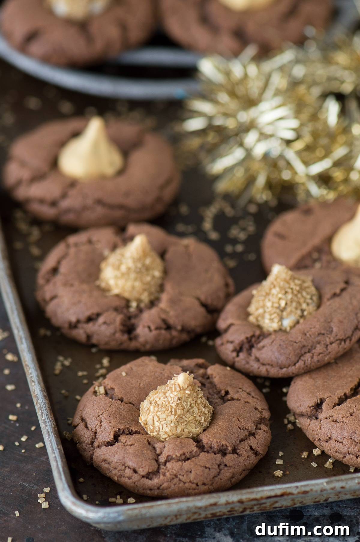 Midnight Kiss Cookies cooling on a metal baking sheet, featuring their unique chocolate peanut butter base and golden Hershey's Kiss toppings.