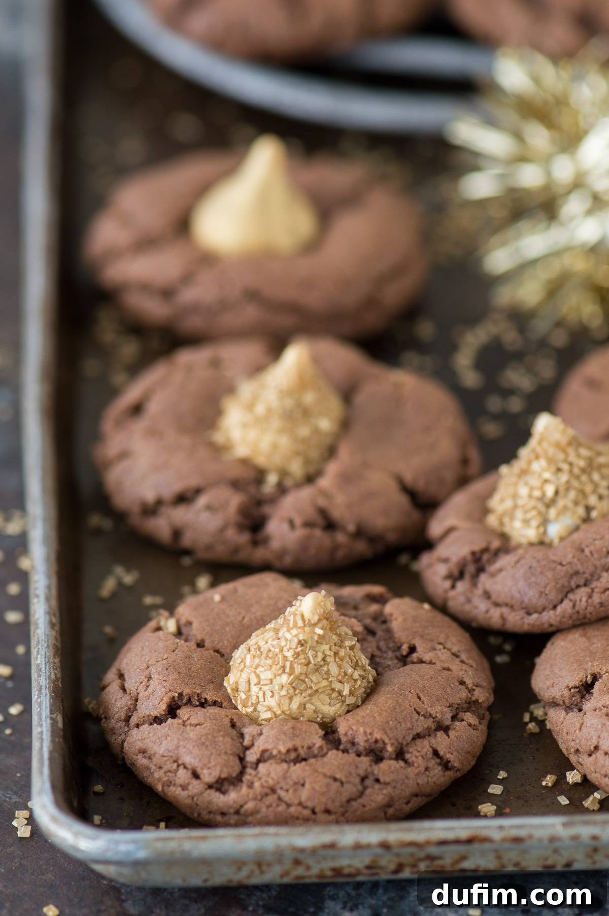 A batch of freshly baked Midnight Kiss Cookies with golden chocolate Kisses, artfully arranged on a baking sheet, ready for a New Year's Eve party.