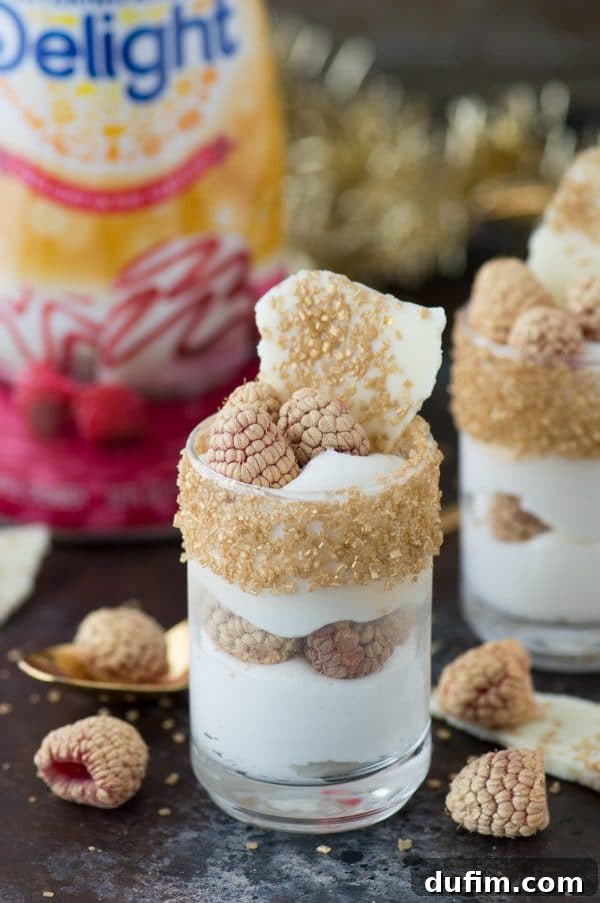 Decadent White Chocolate Raspberry Mousse 6 A beautifully presented white chocolate raspberry mousse dessert, garnished with gold-dusted raspberries and a piece of white chocolate bark, ready for a New Year's Eve party.