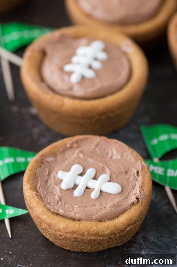 Close-up of a single cheesecake sugar cookie football cup, showing the rich chocolate filling and white icing laces on a dark surface