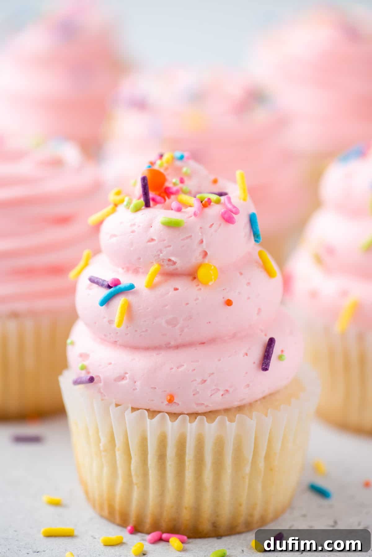 A stunning close-up of several vanilla cupcakes adorned with pink frosting and sprinkles, showcasing their perfect bake and inviting texture.