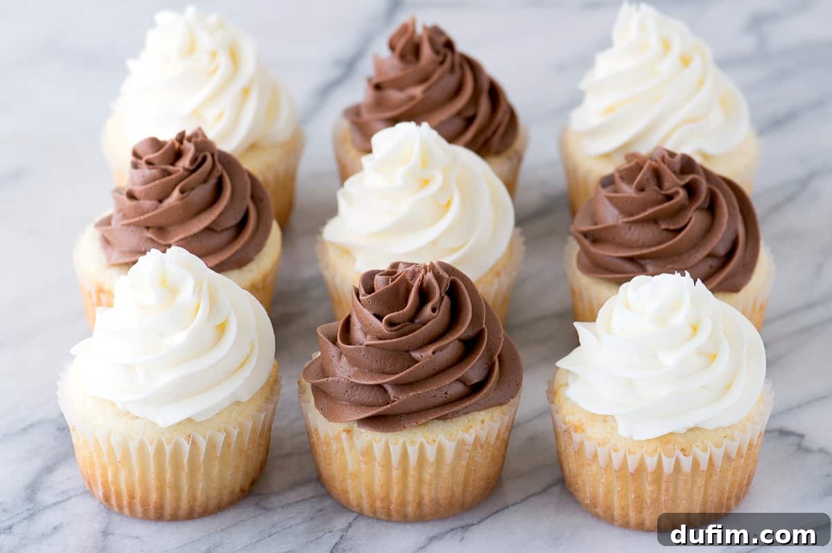A beautifully composed shot of nine vanilla cupcakes, some topped with rich chocolate frosting and others with elegant white frosting, arranged on a marble background.